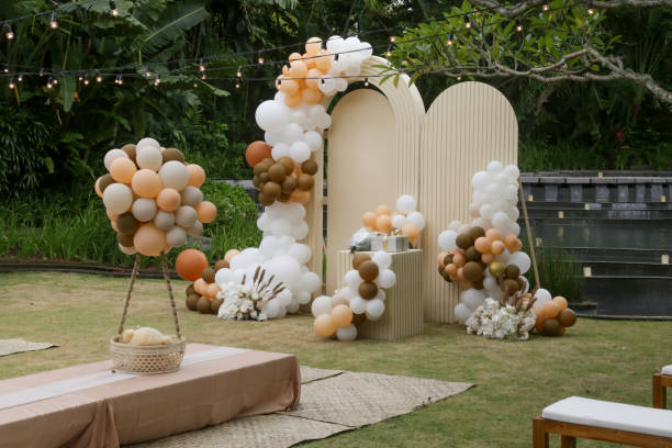 Creative gender neutral baby shower or birthday decoration in the garden. Bohemian style outdoor event set up with balloons. White cream peach caramel balloon arch kit. stock photo
