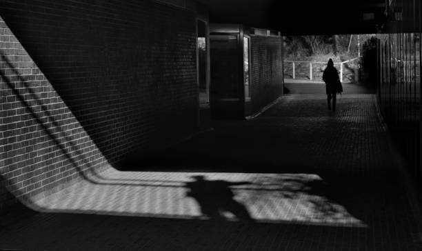 street harasment and me too movement concept, shadow of a man and young girl in a railway station, unrecognizable persons, black and white stock photo