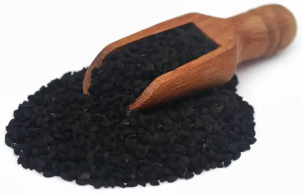 Nigella seeds with wooden scoop, over white background