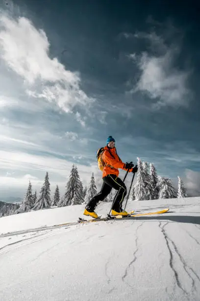 A fully equipped fit woman with proper winter clothes, skis, boots, poles and all other details seen ski touring in the mountains surrounded by mesmerizing nature during a winter vacation.