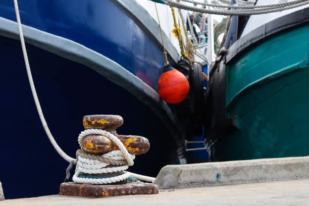 Fishing Boats Tied To Bollard On Harbor Quay Fishing trawler boats tied to metal bollard on quay in harbor mooring line stock pictures, royalty-free photos & images