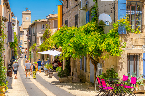 A picturesque main street through the historic medieval town of Saint-Remy de Provence, France, with the colorful shops and cafes and the clock tower in view on a summer day.  Saint-Rémy-de-Provence is a commune in the Bouches-du-Rhône department, Provence-Alpes-Côte d'Azur, Southern France.