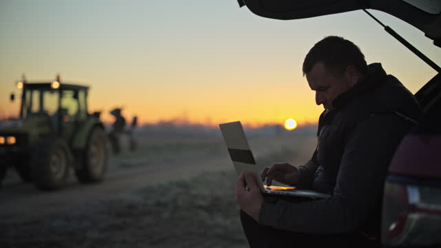 Male farmer using laptop at SUV in rural field at sunrise