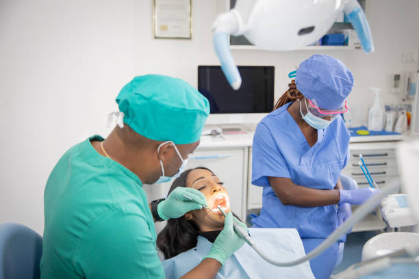 un dentista africano comprueba la salud bucal de su paciente mientras su asistente prepara las herramientas de trabajo - medical exam dentist dentists chair dental assistant fotografías e imágenes de stock