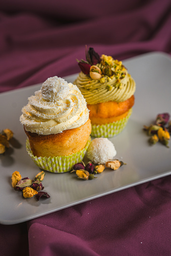 Two deliciously arranged vegan muffins topped with a pile of whipped cream, served on a white ceramic plate and sprinkled with crunchy nuts. High angle view, full length vertical image.
