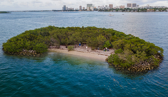 Austin Island with rocky shore on the side and sand shore in the middle at Miami Beach, Florida. Aerial view of a small island with views of the city buildings at the background.