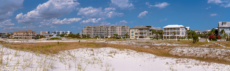 Panorama of beachfront buildings at the beach near Noriego Point in Destin, Florida. Sand dunes with grasses at the front near the multi-storey hotels  apartments against the bright cloudy skies.