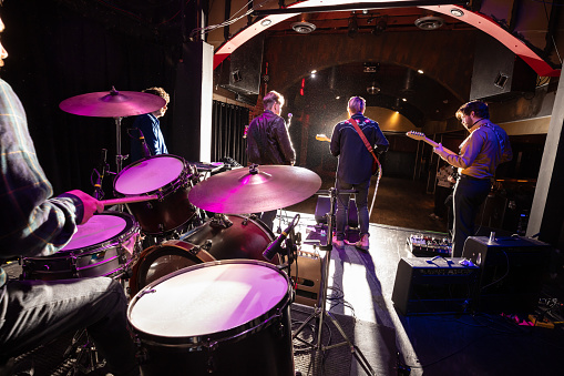 A drummer playing onstage with a rock band during the sound check before a live show at a small venue.