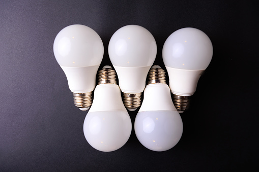 Five white E-27 Edison Screw light bulbs place on a black background and shot from above. Studio shot. No people.