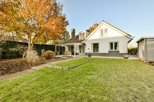 a house in the fall with an orange tree and green grass on the front yard, surrounded by yellow leaves