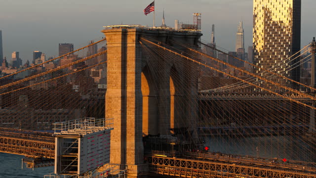Brooklyn Bridge over the East River, with the view of Midtown Manhattan and Manhattan Bridge at the distance in the evening.  Aerial video with the panning-ascending camera motion.