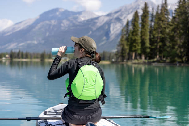 Woman Paddleboarding on Edith Lake, Jasper National Park, Alberta A woman is paddleboarding on Edith Lake in Jasper National Park, Alberta. The turquoise colored lake is very calm. Its is a beautiful sunny summer day in the Canadian Rockies. She is drinking water in a reusable bottle. blue reusable water bottle stock pictures, royalty-free photos & images