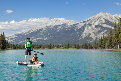 A Mother and son are paddleboarding on Lake Edith in Jasper National Park, Alberta. The turquoise colored lake is very calm. Its is a beautiful sunny summer day in the Canadian Rockies.