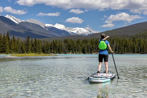 A woman is paddleboarding on Edith Lake in Jasper National Park, Alberta. The turquoise colored lake is very calm. Its is a beautiful sunny summer day in the Canadian Rockies.