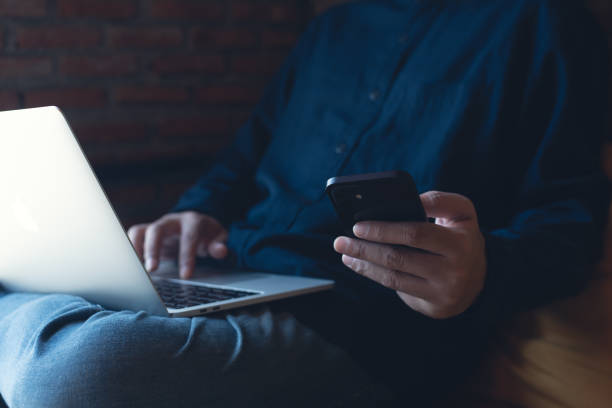 Man freelancer working on laptop and using mobile phone on wooden table at coffee shop, telecommuting