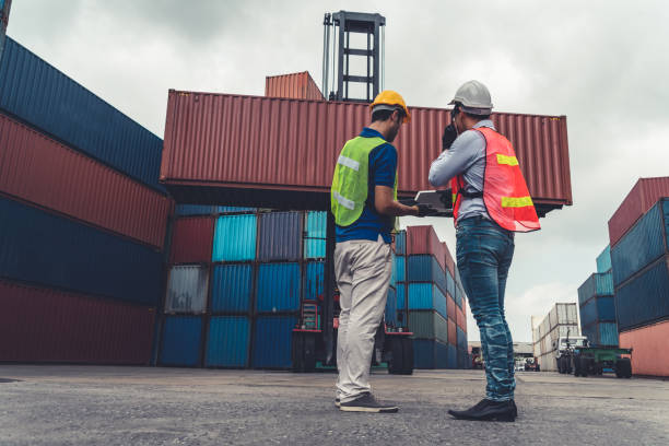 istock Industrial worker works with co-worker at overseas shipping container yard . Logistics supply chain management and international goods export concept . 1464323822