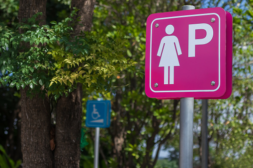 Female or lady parking area sign or symbol with blurred outdoors natural green background.