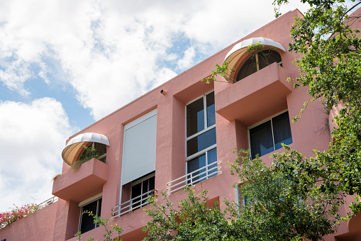 View of a top of residential building with screen and canopies at the balconies in Miami, Florida. Low angle view of an apartment building with balconies facing the trees at the front.