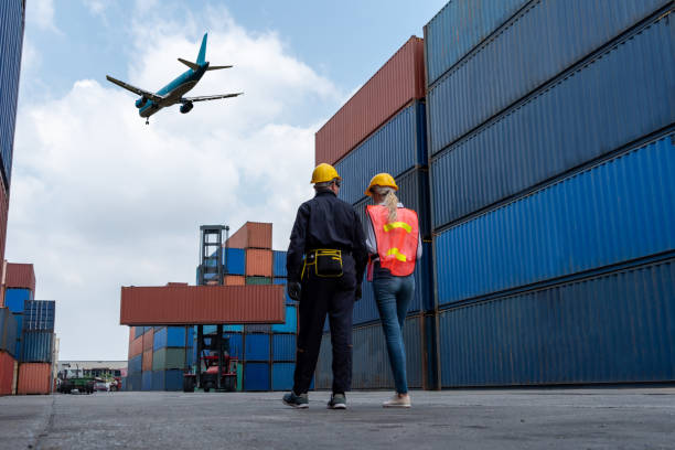 istock Industrial worker works with co-worker at overseas shipping container port . Logistics supply chain management and international goods export concept . 1464332346