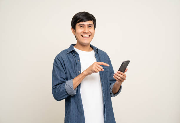 istock Young asian man using smartphone standing on isolated white background. He texting on cell phone. Dressing with jacket and jean. Age around 25. 1464339277