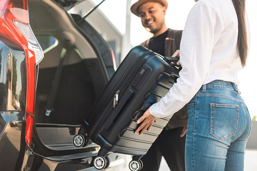 Happy couple puts his suitcase in the back of the car and prepares to leave for honeymoon trip. Husband and wife open the back of the car put luggage travel. Couple moving into new home at moving day