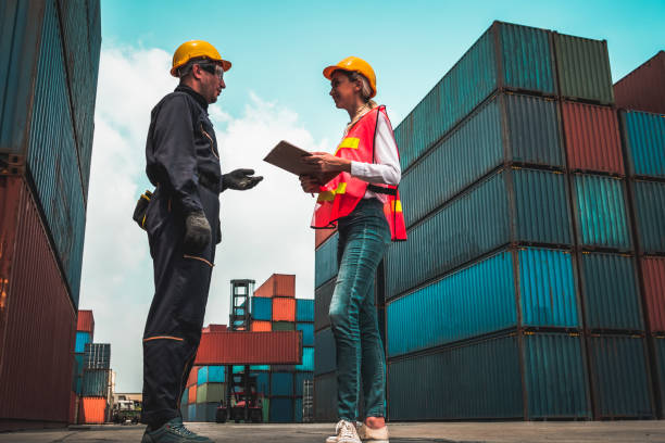 istock Industrial worker works with co-worker at overseas shipping container yard . Logistics supply chain management and international goods export concept . 1464340385