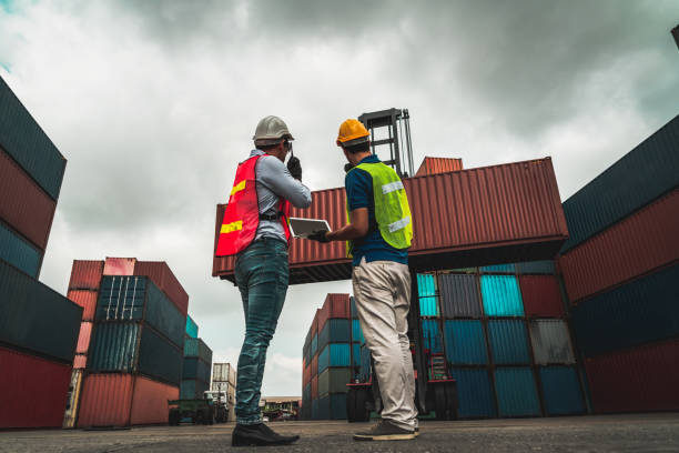 istock Industrial worker works with co-worker at overseas shipping container yard . Logistics supply chain management and international goods export concept . 1464340542