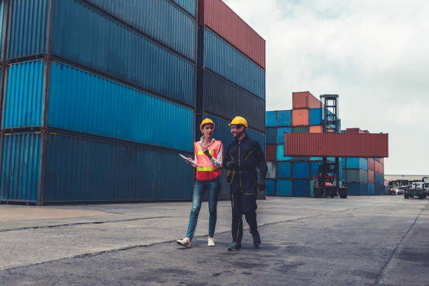 istock Industrial worker works with co-worker at overseas shipping container yard . Logistics supply chain management and international goods export concept . 1464346026