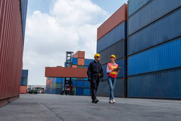 istock Industrial worker works with co-worker at overseas shipping container yard . Logistics supply chain management and international goods export concept . 1464347905