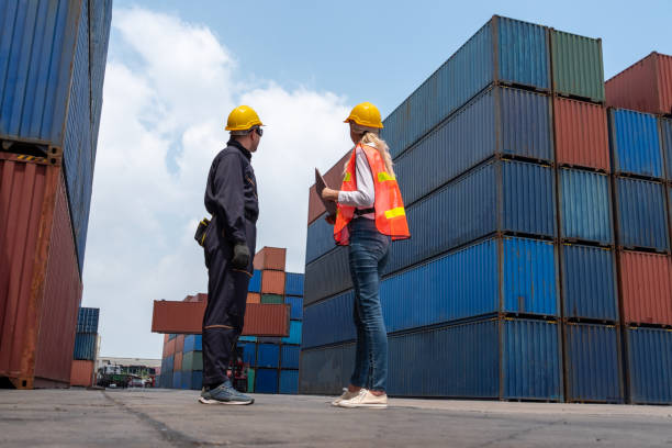 istock Industrial worker works with co-worker at overseas shipping container yard . Logistics supply chain management and international goods export concept . 1464348020