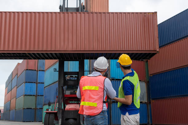 istock Industrial worker works with co-worker at overseas shipping container yard . Logistics supply chain management and international goods export concept . 1464348154