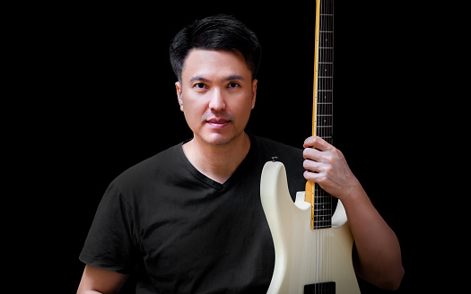 portrait of asian male musician in black t-shirt with white electric guitar, isolated on black