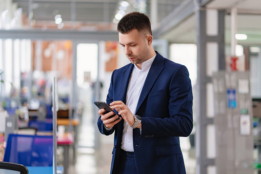 a man in ablue business suit with a phone in hand in the coworking office. the concept of haste or punctuality. the portrait of an entrepreneur. career. office for rent