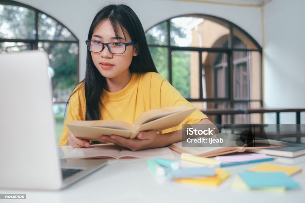 Young Asian female student is preparing to reading a books for exams at university. Young asian university student is reading a books for exams. The college student self learning and studying online in a study room at university. Internet Stock Photo
