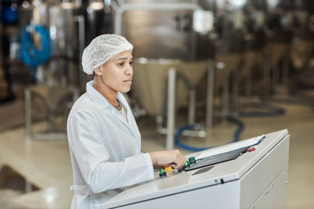 istock Female worker wearing lab coat using control panel at food factory 1464359209