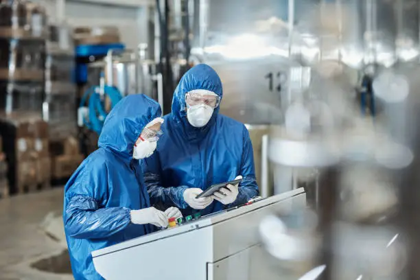 Photo of Two workers wearing protective gear operating equipment at industrial factory