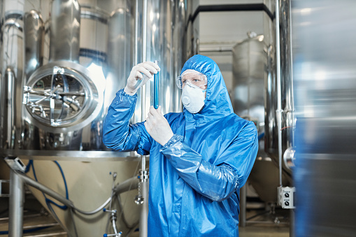 Waist up portrait of worker wearing protective gear and holding test tube at chemical plant