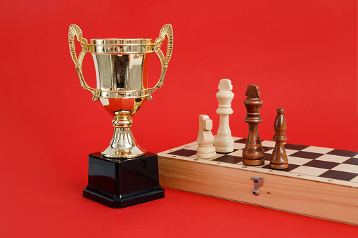 Winner golden cup and Chess board with wooden figures still life on red background