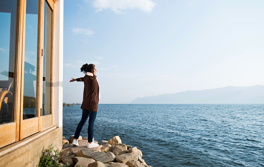 Woman standing by the lakeside with arms outstretched.