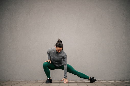 An urban fit sportswoman is warming up on a street downtown.