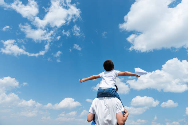 istock Boy sitting on father's shoulder playing paper airplane 1464364379