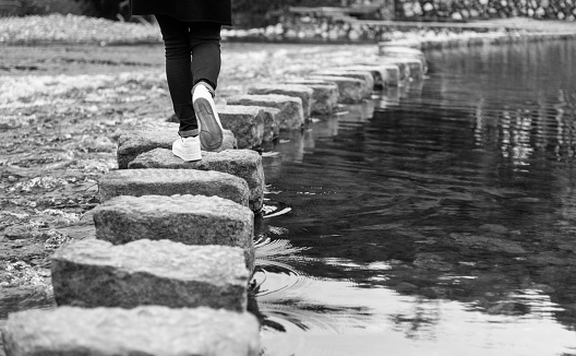 Woman crossing a river on stepping stones.