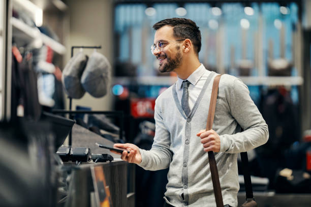 um homem feliz está usando o telefone celular para compra sem dinheiro em boutique. - shopping bag fotos - fotografias e filmes do acervo