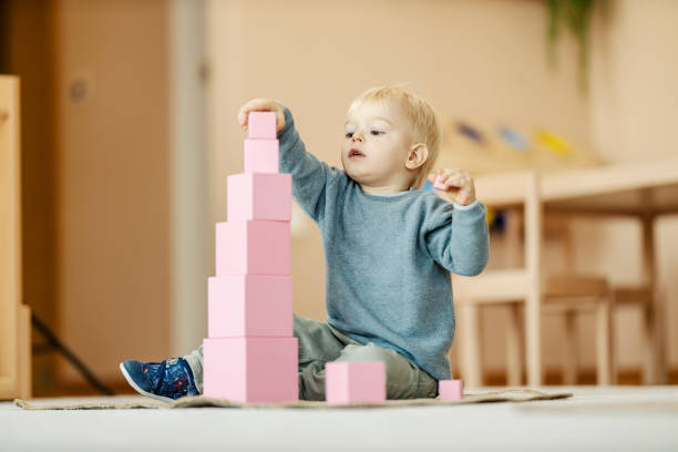 A focused child is putting blocks and making tower at montessori kindergarten. Learning through the game.