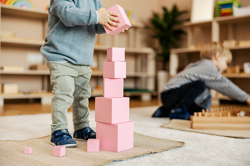 A toddler is learning trough the game. Toddler is building a tower made of wooden blocks at kindergarten.