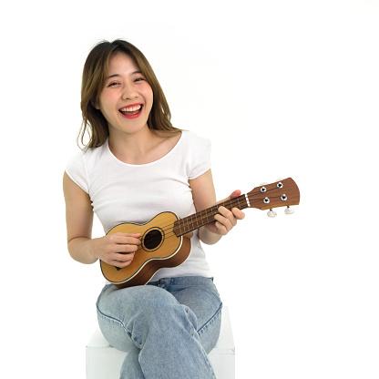 Young asian woman in white t-shirt and jean playing an Ukulele guitar. Portrait on white background with studio light.
