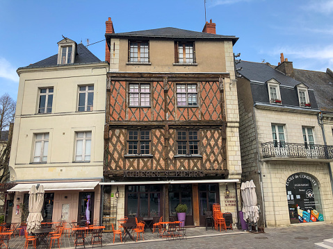 Horizontal cityscape photo of several buildings, some with traditional woodwork facades, a cafe, residential and shops in the main square of the old city centre. Saumur, Loire Valley, Maine et Loire Department, Western France.