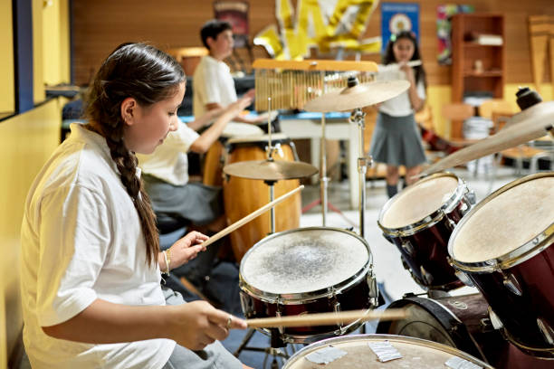 istock Hispanic schoolgirl playing drums with student music group 1464386339