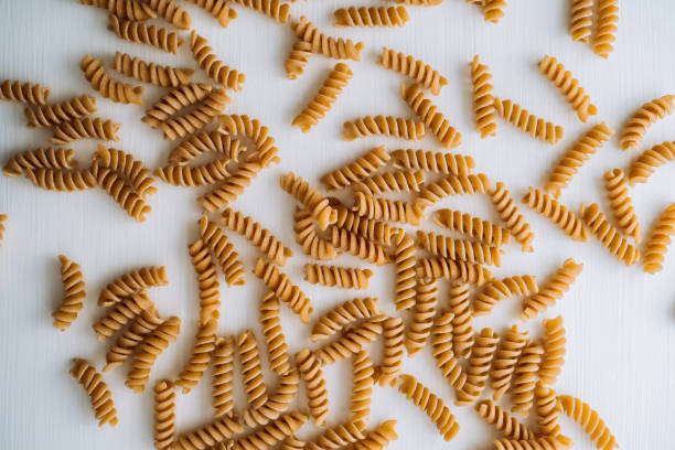 istock Flat lay of scattered many wavy pasta from whole wheat flour on white table 1464387606