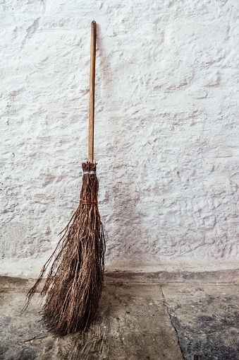 A Witches broom propped up against a white washed wall